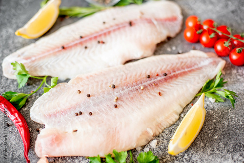 Fresh raw white fish fillet Pangasius with spices and lemon on a stone background.