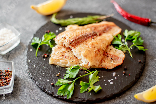 Photo Baked white fish fillet Pangasius with spices and lemon on a stone background