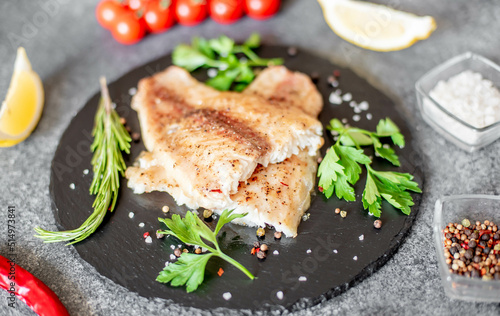 Baked white fish fillet Pangasius with spices and lemon on a stone background