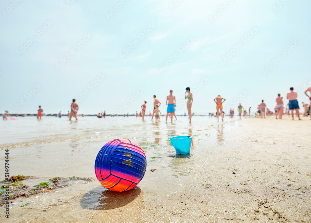 Obraz premium Beach volley ball on an Italian beach on a sunny summer morning with people in the back as they cool off by the sea. Beach ball by the Adriatic sea, Italy.