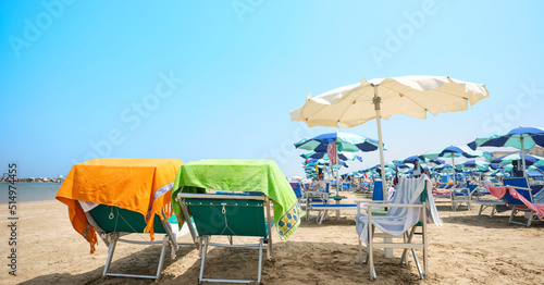 Fototapeta Naklejka Na Ścianę i Meble -  Beach bed with colorful towel in the foreground on a sunny summer day. In the background, the beach equipped with deck chairs and umbrellas on the shores of the Adriatic Sea in Italy.