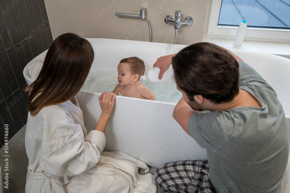 Woman and man crouched washing baby in bathroom Woman and man crouched washing baby in bathroom
