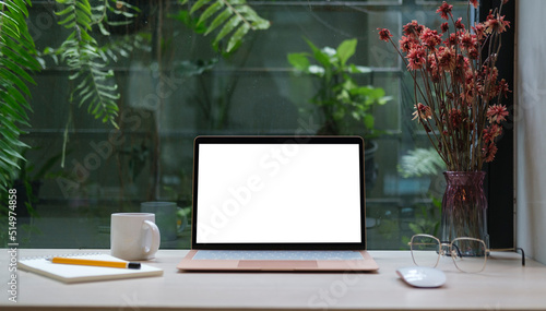 Computer laptop with empty display, coffee cup, pencil holder and houseplant on wooden table..