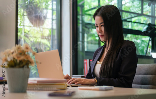 Charming young businesswoman working with laptop computer while sitting in bright modern office..