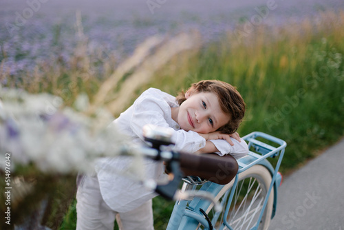 Romantic portrait of an adorable child. A boy with a bouquet and a bicycle in countryside. Summertime childhood and happiness. Walk in nature. Beautiful sunset. School holidays. purple field. Meadow