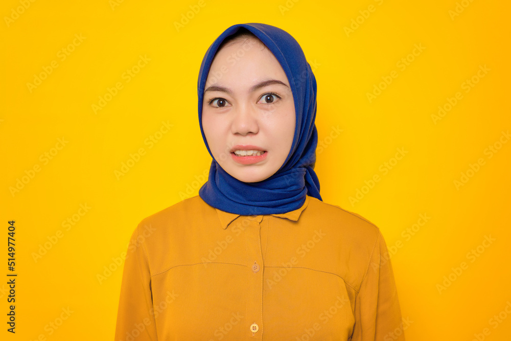 Annoyed young Asian Muslim woman dressed in orange shirt looking at camera and reacting to bad news isolated on yellow background Annoyed young Asian Muslim woman dressed in orange shirt looking at camera and reacting to bad news isolated on yellow background