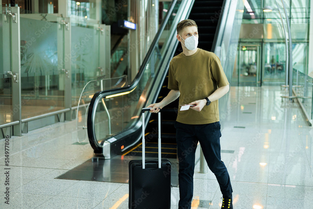Obraz premium A man wearing face mask while standing and carrying suitcase in airport. New normal traveling during a pandemic. Male passenger traveling. Wearing FFP2 mask in aircraft cabin. Safety travel Covid-19