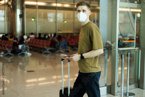 A man wearing face mask while standing and carrying suitcase in airport. New normal traveling during a pandemic. Male passenger traveling. Wearing FFP2 mask in aircraft cabin. Safety travel Covid-19 
