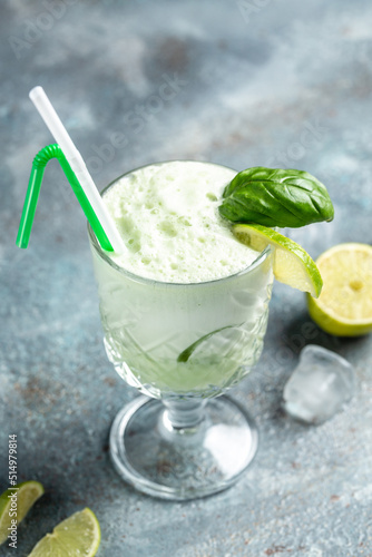 Basil gin alcoholic cocktail. Long alcohol drink with fresh basil leaves and limes, in highball glasses on concrete stone background. vertical image. place for text photo