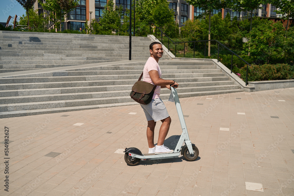 Joyous young male person stepping on e-scooter Joyous young male person stepping on e-scooter