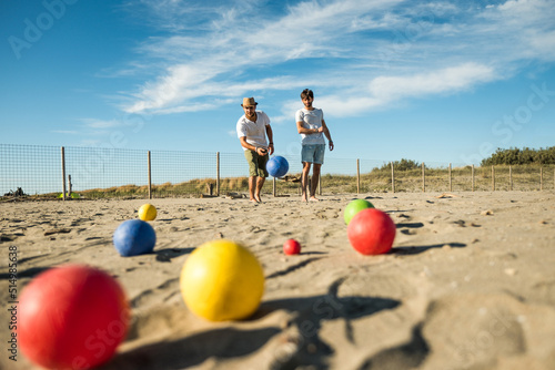 Tourists play an active game, petanque on a sandy beach by the sea - Group of young people playing boule outdoors in beach holidays - Balls on the ground photo