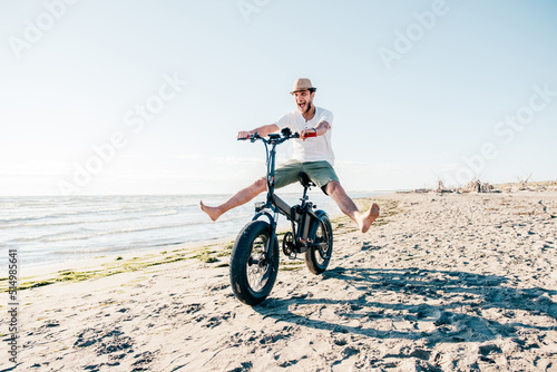 Young man on bicycle having fun with electric bike - carefree boy having fun and smiling on bicycle on the beach on a sunny day - freedom concept