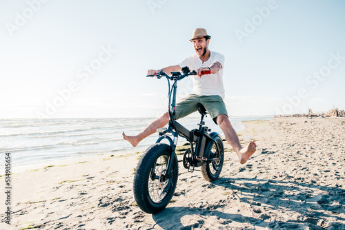 Young man on bicycle having fun with electric bike - carefree boy having fun and smiling on bicycle on the beach on a sunny day - freedom concept