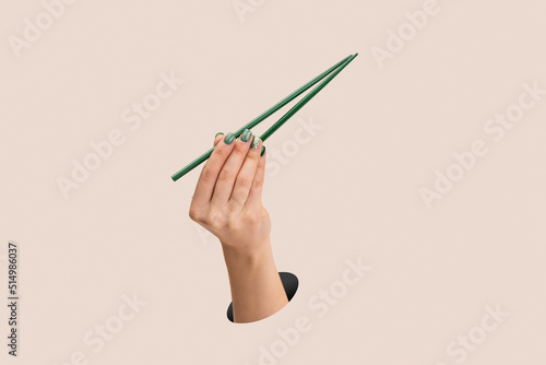 Fotografia Female hand holding green chopsticks upright on clean pink background