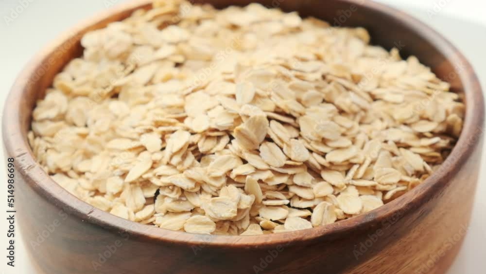 Raw dry oatmeal pouring in wooden bowl, closeup. Raw dry oatmeal pouring in wooden bowl, closeup.