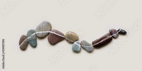 Top view still life with close-up sea stones on sand background, pebbles united by one row as wave. Row from natural stone. Minimal style flat lay, concept of calm, peace, meditation