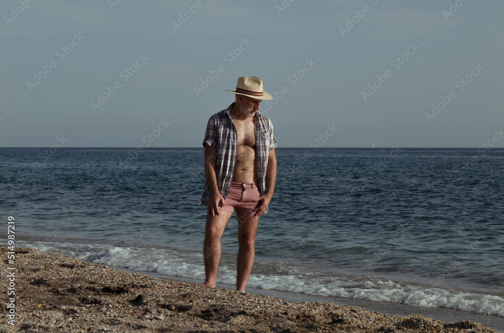 Adult man in hat with open shirt on beach against sea and sky