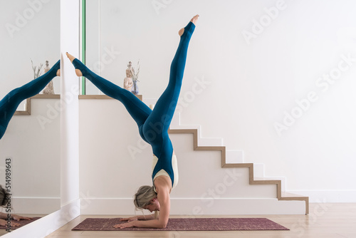 young woman practicing yoga poses stretching in white studio with mirror