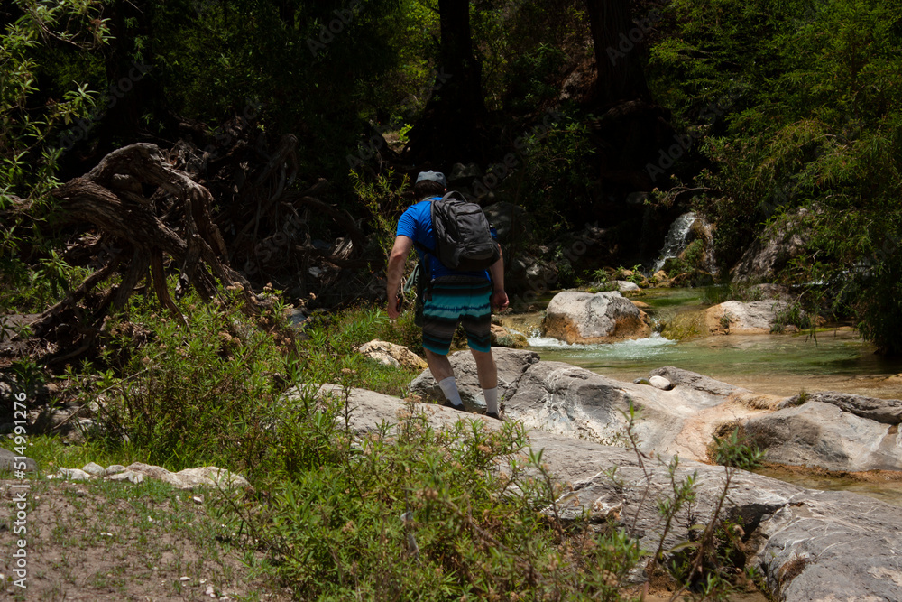 Man walks in complicated topology full of rocks in river bank called avocado doing adventure tourism carrying a backpack and his cell phone in his hand