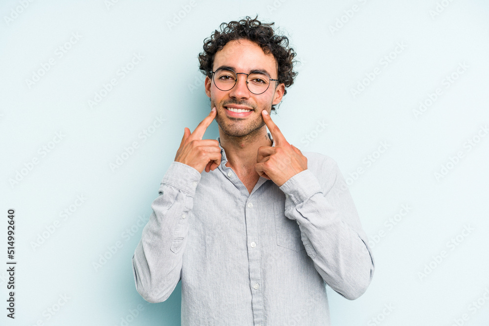 Young caucasian man isolated on blue background smiles, pointing fingers at mouth. Young caucasian man isolated on blue background smiles, pointing fingers at mouth.