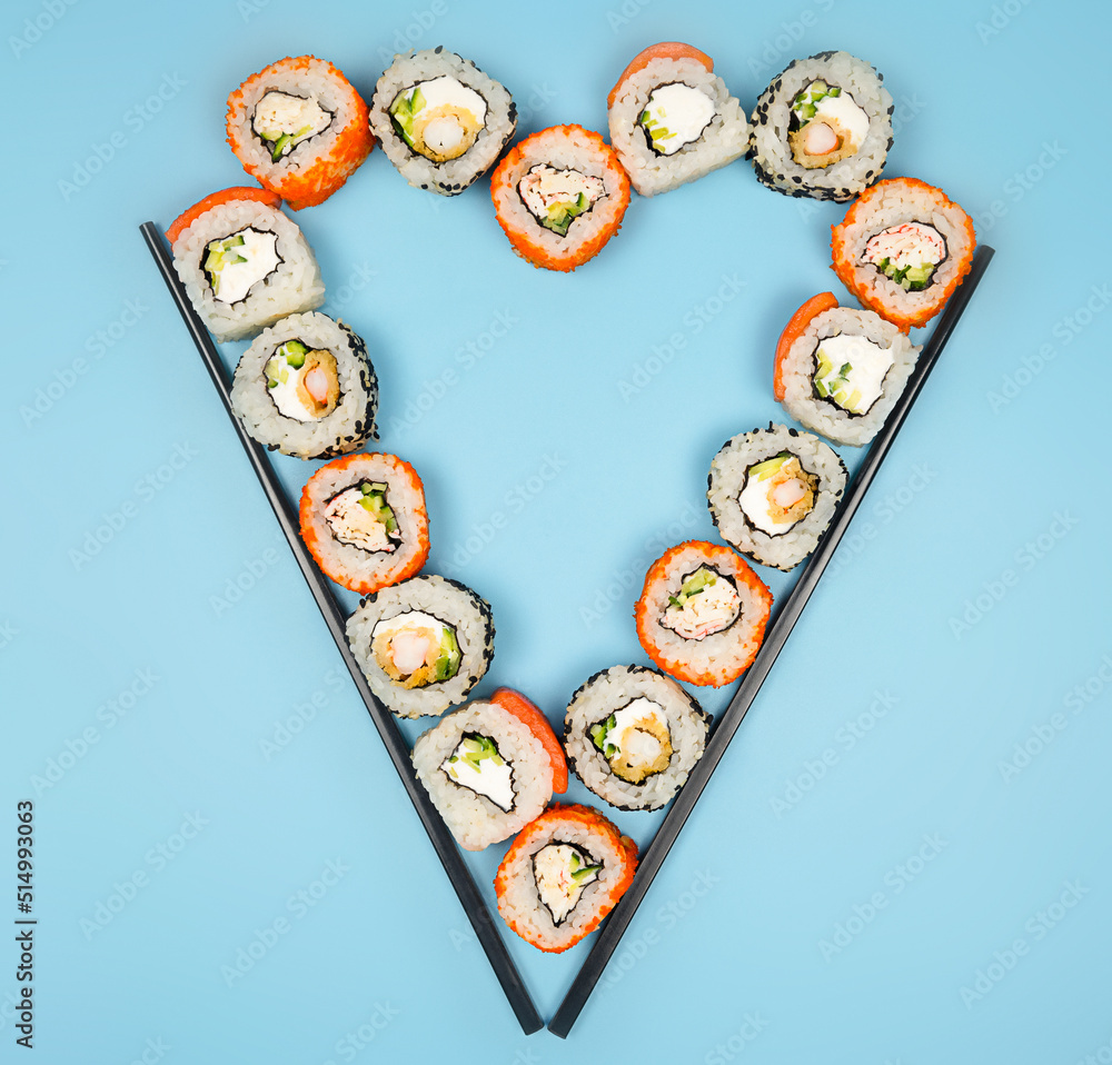 Sushi set and rolls with sticks served as heart on blue background