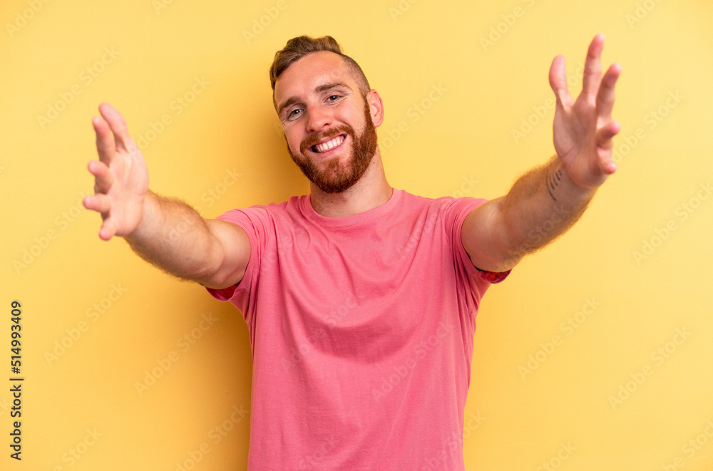 Young caucasian man isolated on yellow background feels confident giving a hug to the camera. Young caucasian man isolated on yellow background feels confident giving a hug to the camera.