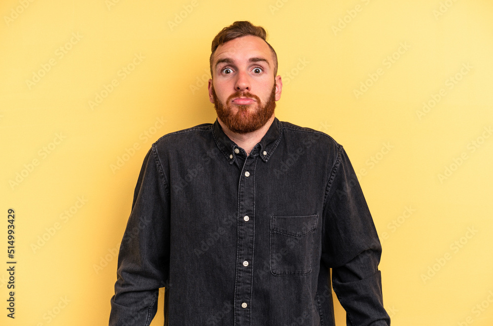 Fototapeta premium Young caucasian man isolated on yellow background shrugs shoulders and open eyes confused.