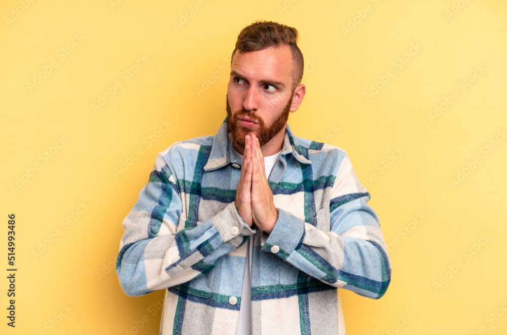 Young caucasian man isolated on yellow background praying, showing devotion, religious person looking for divine inspiration. Young caucasian man isolated on yellow background praying, showing devotion, religious person looking for divine inspiration.