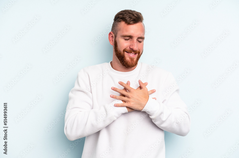 Young caucasian man isolated on blue background laughing keeping hands on heart, concept of happiness. Young caucasian man isolated on blue background laughing keeping hands on heart, concept of happiness.