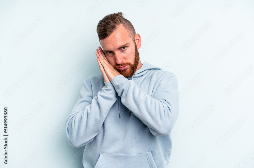 Young caucasian man isolated on blue background yawning showing a tired gesture covering mouth with hand. Young caucasian man isolated on blue background yawning showing a tired gesture covering mouth with hand.