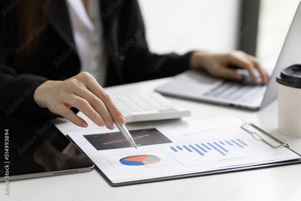 Fototapeta premium Businesswoman holding pen pointing at company sales report financial documents to analyze financial planning and growth marketing.