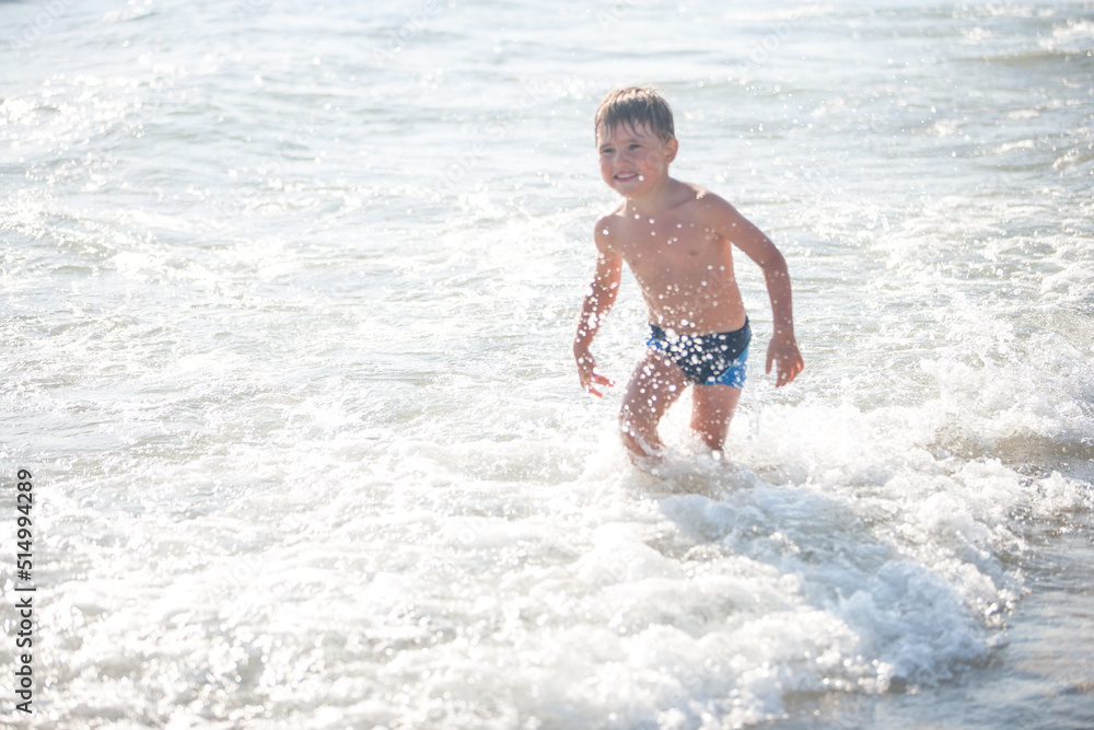 A little boy on the beach, playing with the waves, summer time. Concept of relaxation and a healthy lifestyle
