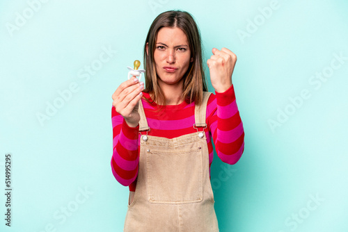 Young caucasian pregnant woman isolated on blue background showing fist to camera, aggressive facial expression. © Asier