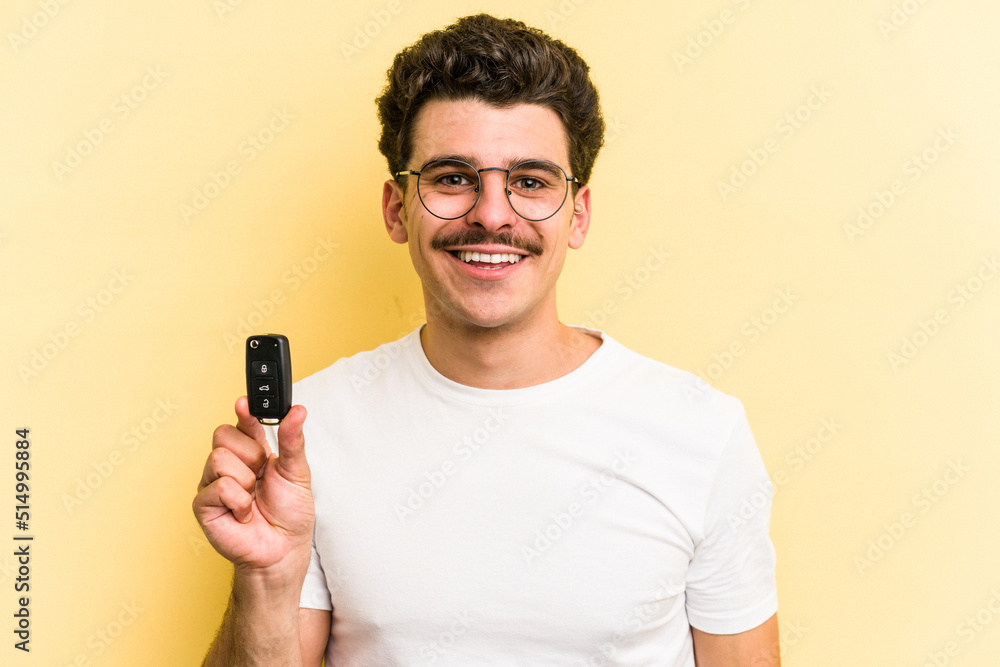 Young caucasian man holding car keys isolated on yellow background happy, smiling and cheerful. Young caucasian man holding car keys isolated on yellow background happy, smiling and cheerful.