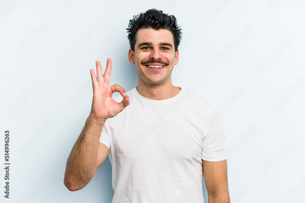 Young caucasian man isolated on blue background cheerful and confident showing ok gesture. Young caucasian man isolated on blue background cheerful and confident showing ok gesture.