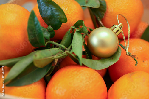 Closeup of a golden Christmas ball and fresh ripe orange tangarines (mandarins) with green leaves. New year, winter holidays concept background