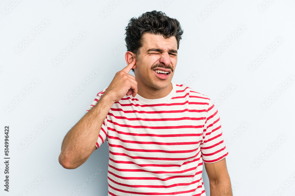 Young caucasian man isolated on blue background covering ears with fingers, stressed and desperate by a loudly ambient. Young caucasian man isolated on blue background covering ears with fingers, stressed and desperate by a loudly ambient.