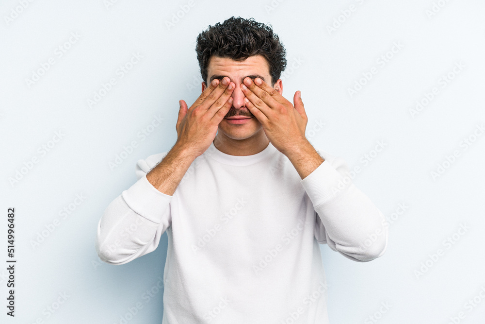 Young caucasian man isolated on blue background afraid covering eyes with hands. Young caucasian man isolated on blue background afraid covering eyes with hands.