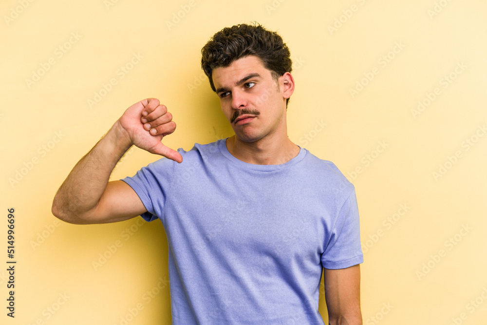 Young caucasian man isolated on yellow background showing a dislike gesture, thumbs down. Disagreement concept. Young caucasian man isolated on yellow background showing a dislike gesture, thumbs down. Disagreement concept.