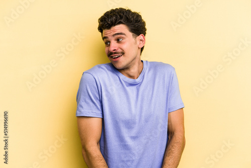 Young caucasian man isolated on yellow background laughs and closes eyes, feels relaxed and happy. © Asier