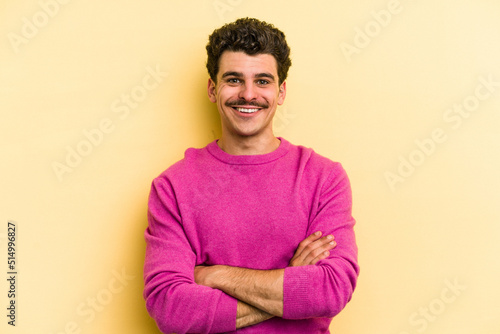 Young caucasian man isolated on yellow background who feels confident, crossing arms with determination.