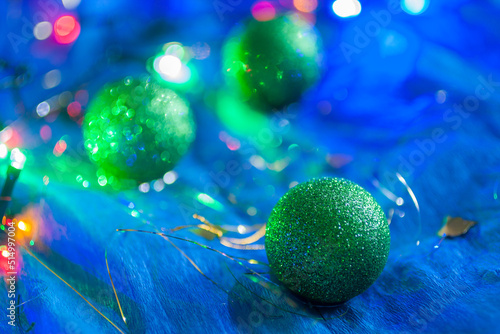 Closeup of the green glittering Christmas ball with another two decorations on the bright blue background. New year, winter holidays cozy atmosphere	