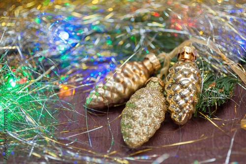 Three golden cones (ceramic Christmas decorations) on the branch of spruce with the colorful garland and tinsel. New year, winter holidays concept background 