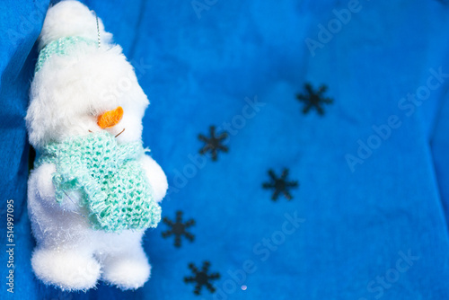 Closeup of a soft toy in a form of a snowman on the blue backround with silver snowflakes. Top view. New Year, Christmas background with the free space for text