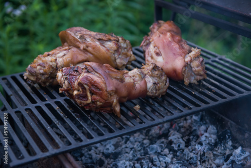Several traditional Bavarian German roasted pork knuckles slowly cooked at rotating broiling rack grill spit, close up, low angle side view. barbecue. the concept of cooking on an open fire.