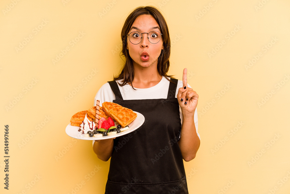 Young hispanic dependent woman holding waffles isolated on yellow background having some great idea, concept of creativity. Young hispanic dependent woman holding waffles isolated on yellow background having some great idea, concept of creativity.