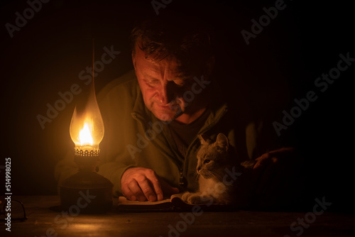 Quadro em tela Man reads a book by the light of a kerosene lamp and a domestic cat lies nearby