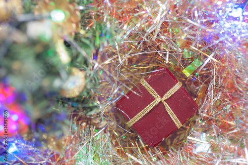 Maroon gift box with golden ribbon and colorful garland on a golden tinsel background. Top view. Christmas atmosphere, New year mood, winter holidays