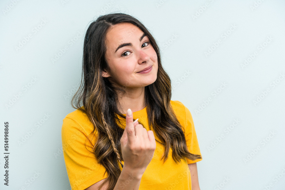 Young caucasian woman isolated on blue background pointing with finger at you as if inviting come closer. Young caucasian woman isolated on blue background pointing with finger at you as if inviting come closer.