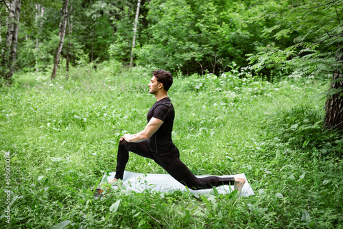 Handsome man in black sportswear doing stretching on nature